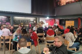 Group of people sitting in the lobby of the Queen's Film Theatre sitting a several different tables talking.